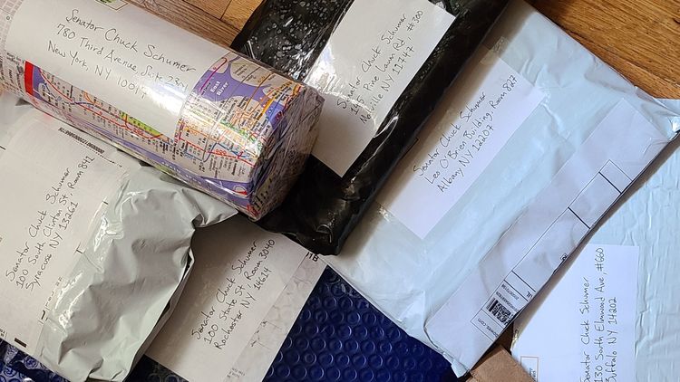 padded envelopes addressed and ready to mail, plus one cylindrical package wrapped in an NYC map