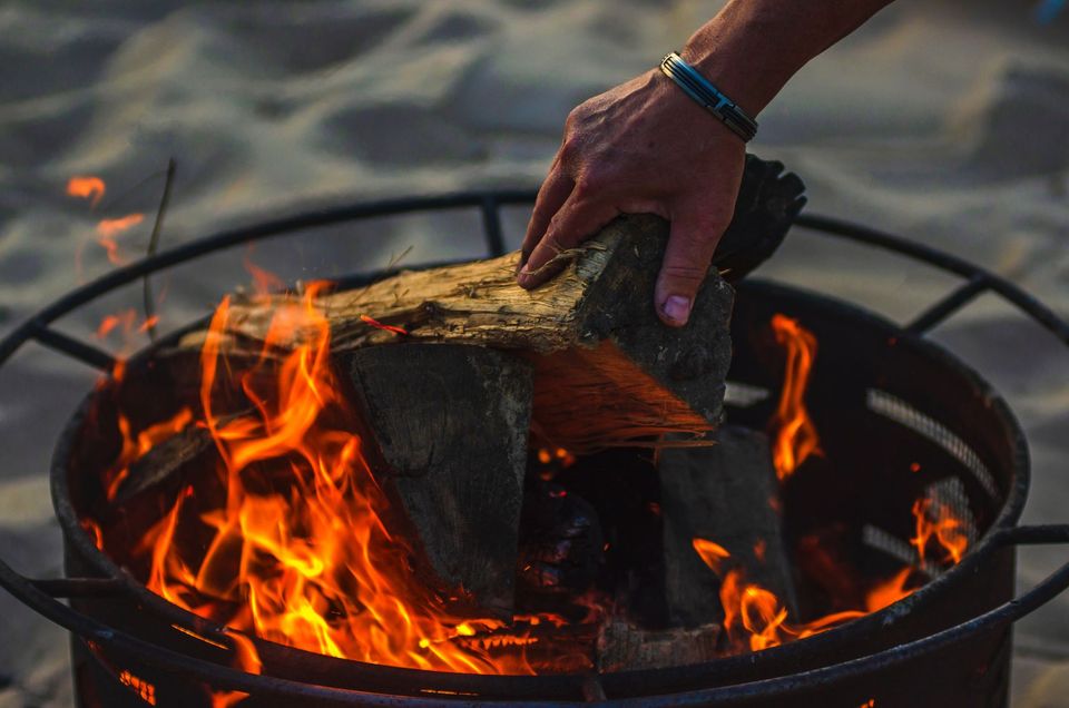 A person's hand putting a firewood in a bonfire