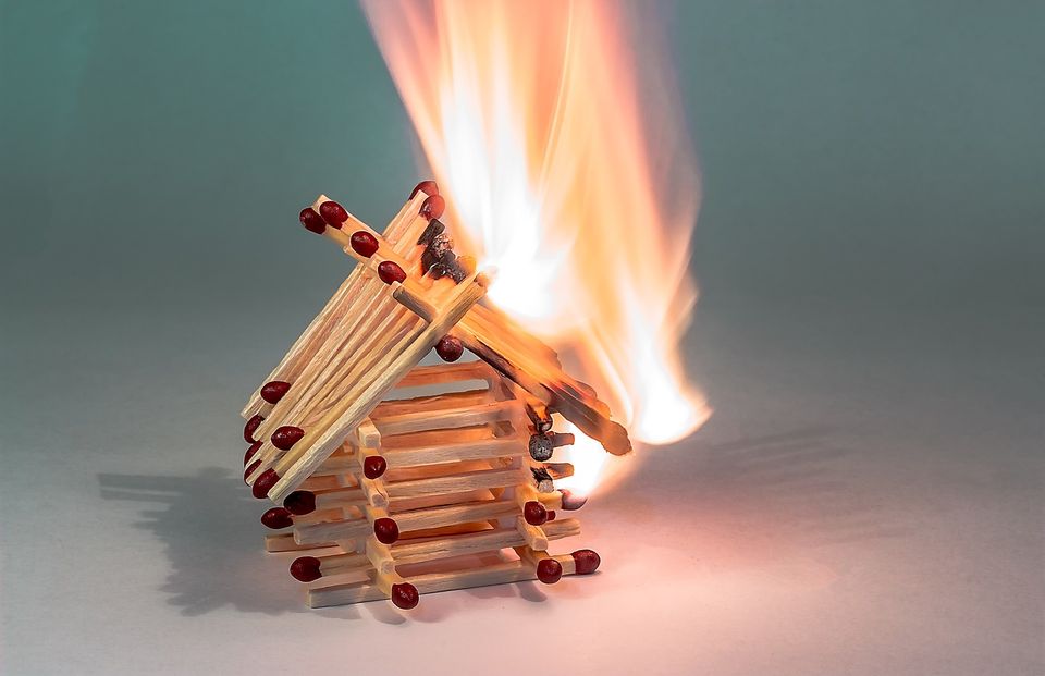 photo of a little house constructed of matches, lit on fire